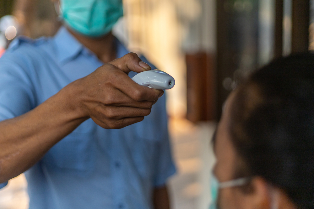 Covid-19 controlling system at a factory. A security guard is using infrared thermometer measuring temperature with worker